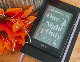 A kindle displaying the cover of One Night Only next to a vase and orange flowers